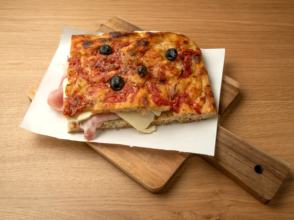 Focaccia Rossa mit Tomaten, Oliven, Schinken und Käse auf dem Holzbrett
